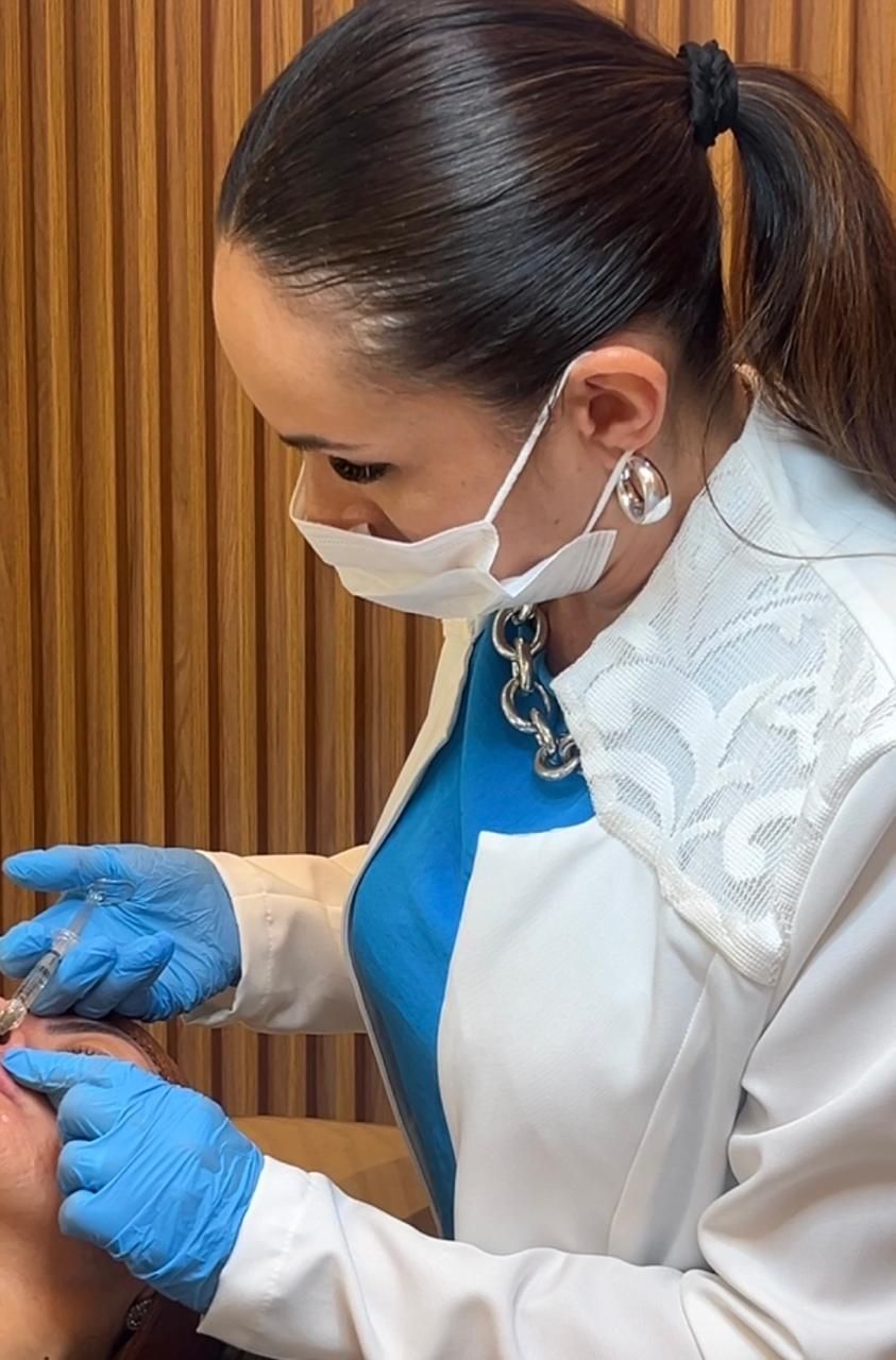 Dra. Aline realizando um procedimento injetável com luvas e máscara